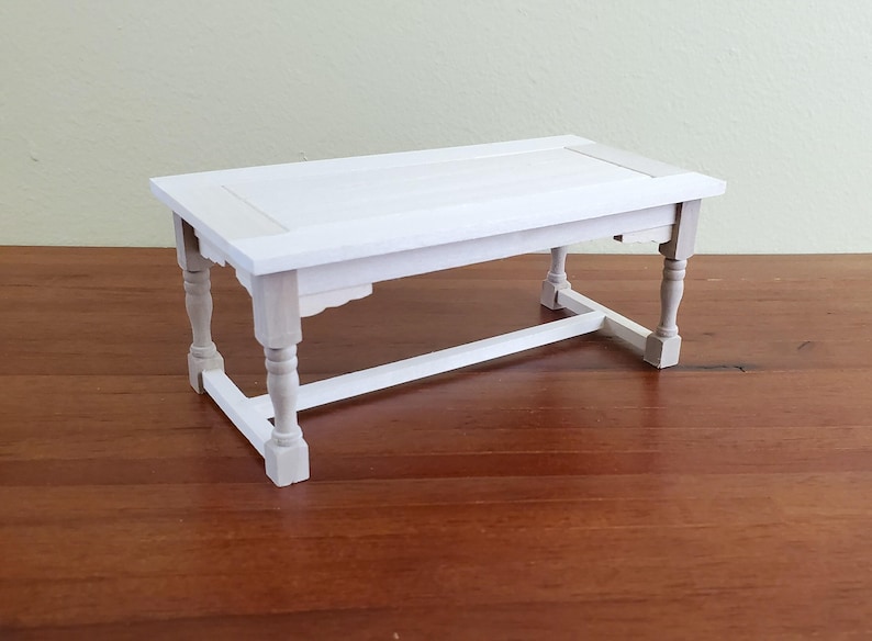 Op de afbeelding: Een kleine, witte houten tafel met een rechthoekig blad en gedraaide poten. De tafel is ongeveer 30 cm lang, 15 cm breed en 15 cm hoog. De tafel is wit geschilderd en heeft een eenvoudig, elegant ontwerp.