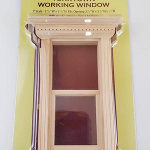 May include: A miniature Yorktown working window, model #5001, made of light-coloured wood. The window has a rectangular shape with two panes and is packaged on a yellow and white card. The text "Houseworks" is visible.