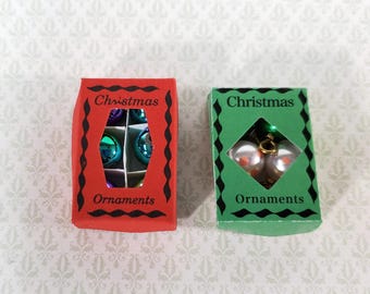 Könnte beinhalten: Zwei rechteckige Schachteln mit der Aufschrift Christmas Ornaments. Die rote Schachtel enthält kleine, glänzende, mehrfarbige kugelförmige Ornamente. Die grüne Schachtel hat einen rautenförmigen Ausschnitt mit zwei weißen Kugeln.