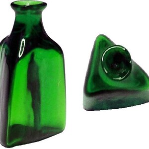 May include: A green glass bottle and a matching triangular stopper. The bottle has a rectangular shape with a narrow neck. The stopper has a circular top. Both items have a dark green and black color scheme.