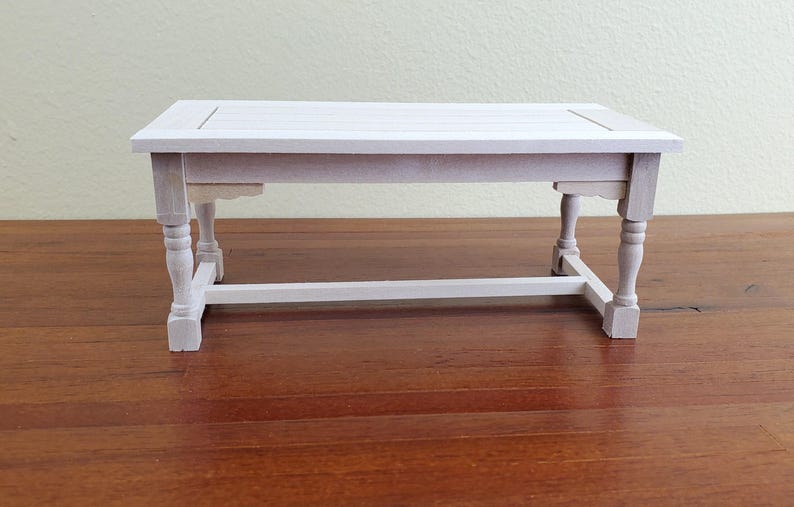 Op de afbeelding: Een kleine, witte houten tafel met een rechthoekig blad en vier gedraaide poten. De tafel is ongeveer 61 cm lang, 30 cm breed en 25 cm hoog. De tafel is een miniatuurmeubelstuk.