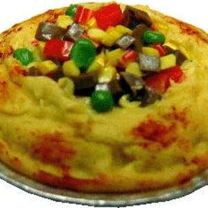May include: A baked dish with a golden-brown crust and a filling of colourful diced vegetables. The vegetables include red, green, yellow, and brown pieces, arranged on top of a creamy, yellow base. The dish sits in a silver foil pie plate.