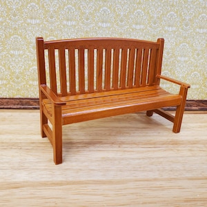Peut inclure: Un banc miniature en bois de couleur brun rougeâtre. Il présente un dossier incurvé, une assise à lattes et des accoudoirs. Ce petit banc est conçu pour une maison de poupée ou un cadre miniature, environ 10 cm de long.