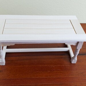 Op de afbeelding: Een kleine, rechthoekige witte houten tafel met een lattenbodem en sierlijke poten. De tafel is ongeveer 46 cm lang, 30 cm breed en 25 cm hoog. Hij staat op een donkerbruin houten oppervlak.
