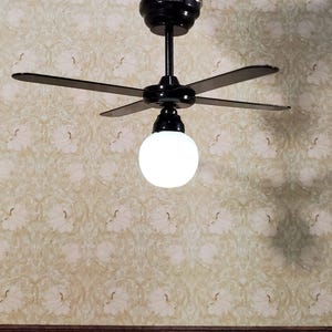 May include: Black ceiling fan with four blades and a white globe light fitting. The fan is mounted on a ceiling with floral patterned wallpaper.