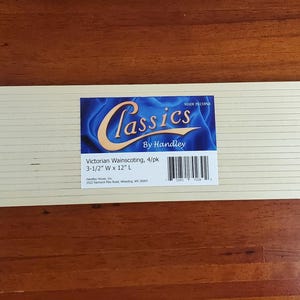 May include: A rectangular piece of light-colored wainscoting with horizontal grooves. A label with the text "Classics by Handley" and product details is affixed to the wainscoting. The dimensions are 3-1/2" W x 12" L.