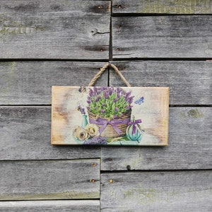 May include: A wooden sign featuring a lavender floral design. The sign has a purple ribbon and the text "Fleur De Lavande" on it.
