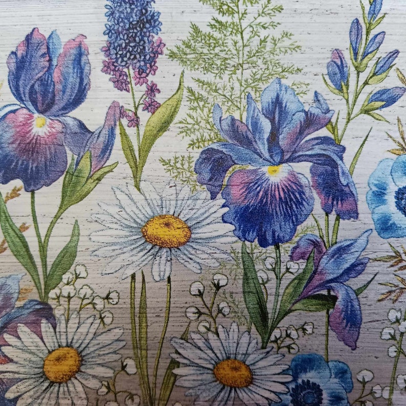 May include: A floral print featuring blue irises, white daisies, and blue anemones on a white background. The flowers are arranged in a random pattern and are surrounded by green leaves.