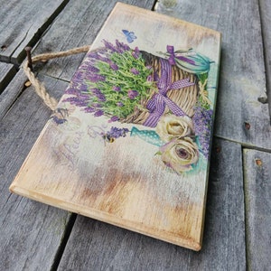 May include: A wooden sign featuring a lavender bouquet in a wicker basket, a butterfly, and the text "Fleur De". The sign has a distressed, rustic look and is ideal for farmhouse decor.