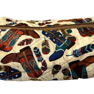 Puede incluir: Una bolsa de tela acolchada de color crema con una cremallera marrón. La bolsa tiene un estampado de botas de vaquero y plumas coloridas en tonos rojos, azules y marrones. Las botas tienen diseños intrincados.