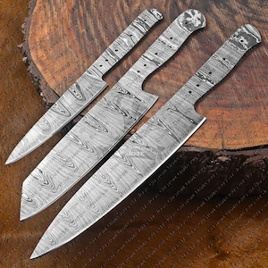 Peut inclure: Trois lames de couteau en acier de Damas avec un motif tourbillonnant distinctif. Les lames ont une conception à soie pleine, avec des trous pour la fixation de la poignée. L'image montre les lames sous différents angles, mettant en évidence le travail du métal.