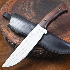 May include: A close-up of a knife with a brown wooden handle and a silver blade. The blade has a pattern of lines and is very sharp. The knife is sitting on a wooden surface and has a black leather sheath.