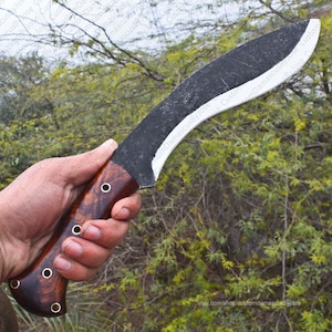 Puede incluir: Un cuchillo grande y curvo con una hoja oscura y texturizada y un mango de madera. El mango es de color marr&oacute;n intenso con vetas de madera visibles y est&aacute; asegurado con remaches met&aacute;licos. La hoja tiene un filo afilado y una forma curva.
