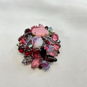 May include: A vintage brooch featuring an array of colorful gemstones in shades of pink, red, and purple. The brooch has a cluster design with various shapes and sizes of stones, creating a sparkling and eye-catching accessory.