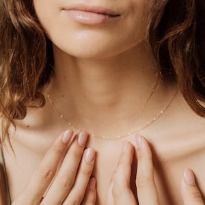 May include: A delicate gold chain necklace worn by a person with their hands near their chest.