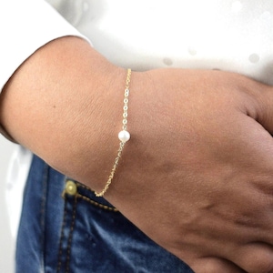 May include: A delicate gold chain bracelet with a single white pearl charm.