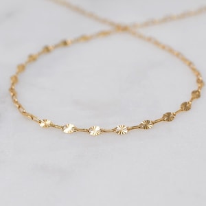 May include: A delicate gold necklace featuring a chain with small, circular, starburst-like charms. The necklace is displayed on a white surface, showcasing its intricate design and warm, golden hue. This piece is ideal for adding a touch of elegance.