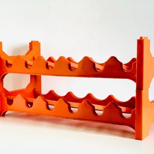 Può includere: Portabottiglie in plastica arancione brillante a due livelli, ciascuno progettato per contenere più bottiglie. Il portabottiglie ha un design geometrico robusto con dettagli ritagliati sui lati e sulla parte superiore, adatto per la conservazione domestica.