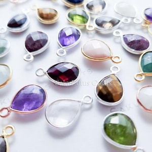 May include: Assortment of gemstone teardrop pendants with gold-plated settings. The pendants are in various colours, including amethyst, clear quartz, green, and pink.