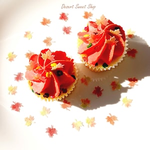 May include: Two cupcakes with red frosting and leaf-shaped decorations on a white plate. The cupcakes have yellow liners and are sprinkled with colorful candies. The image includes the text "Desert Sweet Shop".