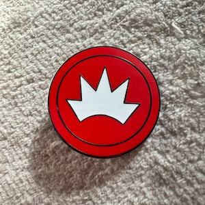 May include: A red and black enamel pin with a white crown design. The crown has five points.