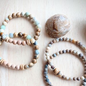 May include: Three beaded bracelets with brown, beige, and blue beads. The bracelets are stacked on a light wood surface.