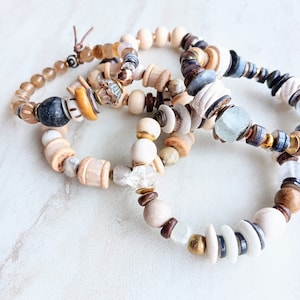 Op de afbeelding: Een set van vier armbanden met verschillende kralen, waaronder witte, bruine, beige, blauwe en gouden. De armbanden zijn gemaakt van natuurlijke materialen en hebben een bohemian stijl.