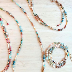 Può includere: Diverse collane di perline di varie lunghezze e design. Le collane presentano un mix di perline colorate, tra cui turchese, rosso, blu e marrone, infilate con catene e chiusure color oro. Le perline sono di forme e dimensioni diverse.