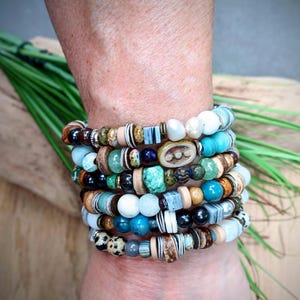 May include: A multi-strand bracelet featuring a diverse collection of beads in various shapes, sizes, and textures. The beads include shades of turquoise, brown, white, black, and tan, with some featuring speckled, striped, and smooth finishes.