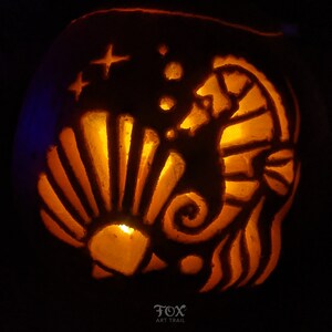 May include: A carved pumpkin with a glowing interior, featuring a seahorse, seashell, and star design. The pumpkin's orange colour contrasts with the dark background. The text "FOX ART TRAIL" is at the bottom.