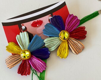 Peut inclure: Un collier de fleurs coloré avec un ruban vert et une paire de boucles d'oreilles assorties. Le collier et les boucles d'oreilles présentent un motif de fleurs multicolores avec un strass jaune au centre.