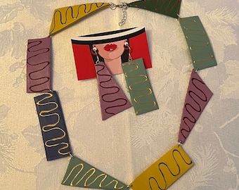 May include: A colorful geometric necklace made of leather with gold accents. The necklace is made up of different shapes and sizes of leather pieces, each with a unique design. The necklace is a statement piece that would add a touch of whimsy to any outfit.