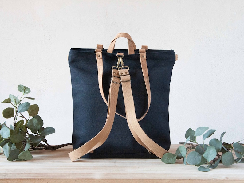 May include: A dark blue canvas backpack with brown leather straps and buckles. The backpack has a top handle and a flap closure.
