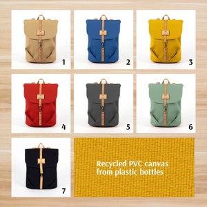 Op de afbeelding: Zeven canvas rugzakken in verschillende kleuren met leren banden en gespen. De rugzakken zijn in een rasterpatroon op een houten oppervlak gerangschikt. De tekst "Gerecyclede PVC canvas van plastic flessen" wordt onder de rugzakken weergegeven.