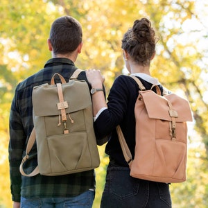 Peut inclure: Deux personnes portant des sacs à dos, l'un vert et l'autre pêche, se promènent dans un parc avec des feuillages d'automne en arrière-plan.