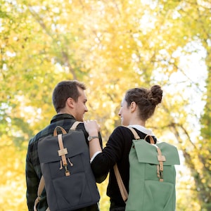 May include: A couple walking in a forest with fall foliage in the background. They are both wearing backpacks, one is green and one is dark blue.