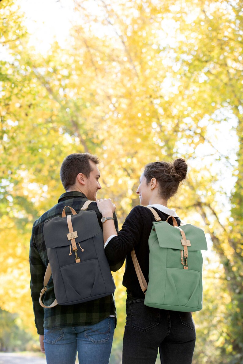 May include: A couple walking in a forest with fall foliage in the background. They are both wearing backpacks, one is green and one is dark blue.