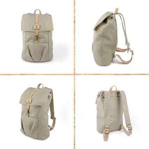May include: A beige canvas backpack with brown leather straps and buckles. The backpack has a flap closure and a front pocket.