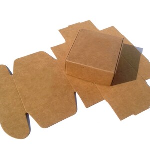 May include: A brown cardboard box with a square base and a flap that folds over the top. The box is unfolded and lying flat on a white surface.