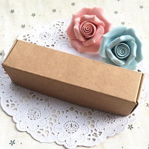 May include: A brown cardboard box with a white lace doily underneath. Two decorative roses, one pink and one light blue, are placed on top of the box.