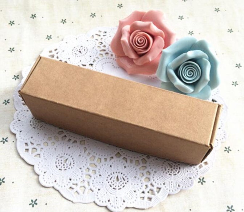 May include: A brown cardboard box with a white lace doily underneath. Two decorative roses, one pink and one light blue, are placed on top of the box.