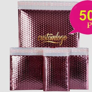 Könnte beinhalten: Eine Reihe von metallisch rosafarbenen Luftpolstertaschen mit strukturierter Oberfläche. Die Versandtaschen haben oben einen weißen und silbernen Klebestreifen. Eine rosa Sprechblase zeigt "50 Stück", und der goldene Text "customlogo" ist ebenfalls sichtbar.