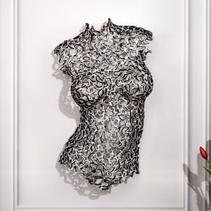 Könnte beinhalten: Eine Wandskulptur eines menschlichen Torsos mit einem komplizierten, durchbrochenen Gitterdesign. Die Struktur besteht aus miteinander verbundenen schwarz-silbernen, metallisch wirkenden Segmenten, die ein komplexes, netzartiges Muster bilden.