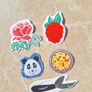May include: Five colourful stickers with cartoon faces. A red raspberry, a pink rose, a blue panda, a yellow pizza, and a black fish.