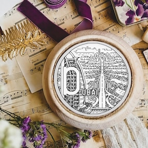 Może przedstawiać: Okrągła drewniana podkładka z czarno-białym rysunkiem panoramy Dubaju. Podkładka leży na stole z nutami, kwiatami i innymi ozdobami.