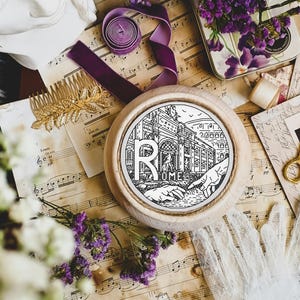 Pode incluir: Um aro de bordado de madeira branco com um desenho em preto e branco de um edifício com a palavra "ROMA" abaixo. O aro é rodeado por flores, partituras musicais e outros itens decorativos.