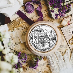 May include: A wooden round embroidery hoop featuring a black and white illustration of the Warsaw skyline. The hoop is surrounded by purple flowers, music sheets, and other decorative items.