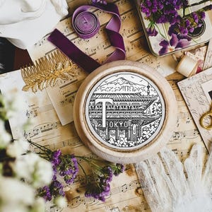 May include: A black and white embroidery hoop with a design of a Japanese temple and the word "TOKYO" in a banner. The hoop is on a table with music sheets, flowers, and other decorative items.