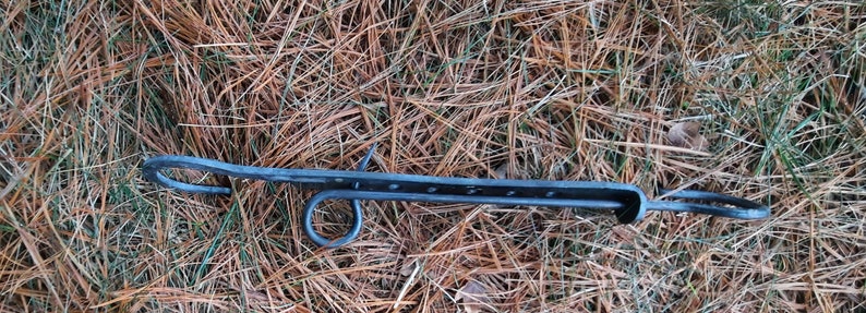 Peut inclure: Un loquet de portail en m&eacute;tal noir avec deux boucles &agrave; chaque extr&eacute;mit&eacute;. Le loquet est pos&eacute; sur un lit d'aiguilles de pin brunes.