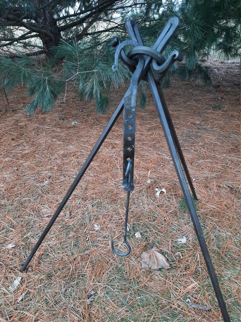 Peut inclure: Un tr&eacute;pied en m&eacute;tal noir avec un crochet et un anneau au sommet. Le tr&eacute;pied est pos&eacute; sur un lit d'aiguilles de pin.
